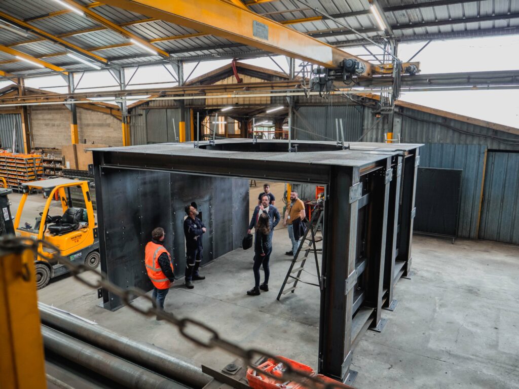 Engineers discussing and inspecting a large metal structure inside an industrial warehouse, highlighting collaborative project planning.
